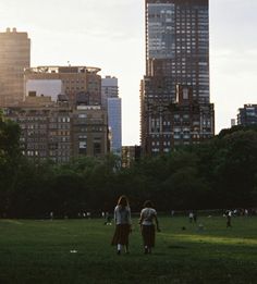 two people are walking through the park in front of tall buildings