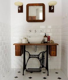 an old fashioned sewing machine is sitting in front of a bathroom sink with two mirrors above it