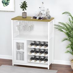 a white bar with wine glasses and bottles on the top shelf next to a potted plant