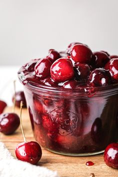 a jar filled with cherries sitting on top of a wooden table next to other cherries