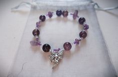 ✹ February Birthstone Amethyst Bracelet✹ ✹This beaded bracelet features a fairy charm alongside purple glass beads and natural amethyst stone beads.  ✹It is beaded on stretch elastic and is approximately 17 cm in length. It stretchs comfortably around the hand to sit on the wrist.  ✹ Amethyst is the birthstone for those born in February. It is a purple variety of quartz and one of the most popular purple stones for jewelry. As it is the birthstone for February, it is also the stone of St. Valentine and represents faithful love. It is heavily associated with calming properties like healing, spiritual awareness, and balance.  Please note all my items are handmade so please handle with care! ♥ This bracelet should be kept out of water as well as extended periods in sunlight (don't leave it in Stones For Jewelry, Born In February, Fairy Charms, Protection Bracelet, Birthstone Gifts, February Birthstone, Amethyst Bracelet, Bracelet Beaded, Glass Beaded Bracelets