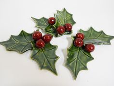 three holly leaves with red berries are on a white table top and one is green