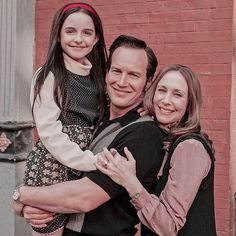 a man, woman and child standing in front of a brick wall smiling for the camera