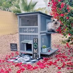 a small dog house in the middle of some red flowers and greenery with a sign that says welcome