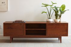 two potted plants sit on top of a wooden entertainment center in front of a white wall