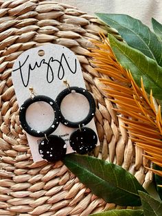 two pairs of black earrings sitting on top of a woven basket next to green leaves