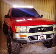 a red toyota pickup truck parked in a garage next to a metal wall with a light on it