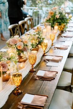 a long table is set with gold and white place settings, candles, and flowers