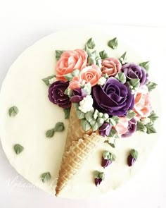 an ice cream cone decorated with flowers on top of a white cake covered in icing