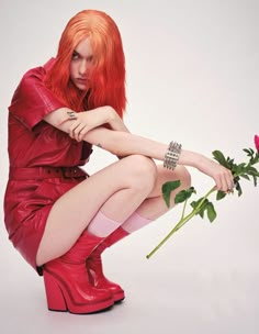 a woman with red hair and boots kneeling down holding a rose in her right hand