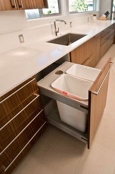 a kitchen area with sink, trash can and cabinets