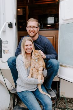 a man and woman are holding a cat in front of an rv door with the doors open