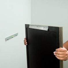 a woman holding up a black piece of paper next to a white wall with a ruler on it