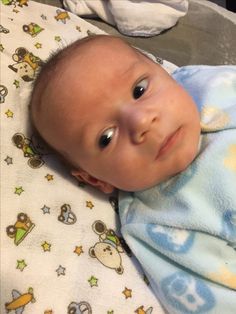 a close up of a baby laying on top of a bed next to a blanket