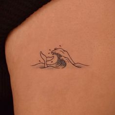 a woman's back with a small wave tattoo on her left side ribcage