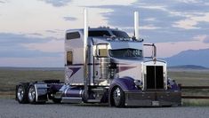 a large semi truck is parked on the side of the road with mountains in the background