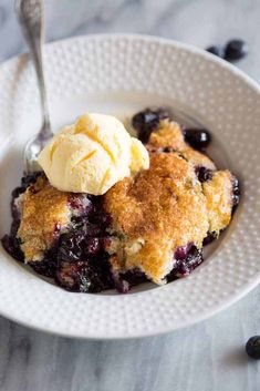 a white bowl filled with blueberry cobbler and ice cream on top of it