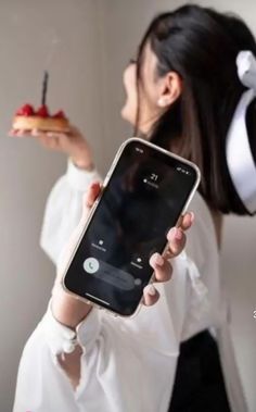 a woman holding up a cell phone in front of her face with a piece of cake on it