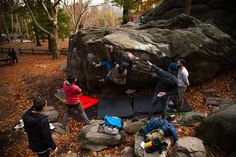 some people are standing around with their arms in the air and one person is climbing up a large rock