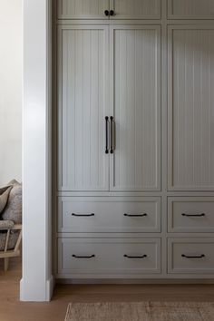 a large white closet with many drawers and cupboards in the corner next to a chair