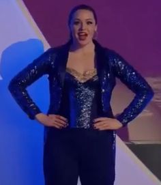 a woman standing in front of a purple and blue background with her hands on her hips