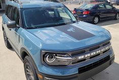 a blue truck parked on the side of a road next to other cars in a parking lot