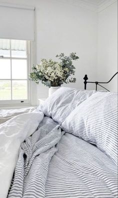 a bed with white sheets and blue striped comforter next to a vase with flowers