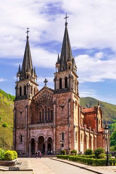 an old church with two towers on the front and one at the top, surrounded by greenery