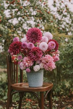 a bucket filled with lots of flowers sitting on top of a wooden chair in front of trees