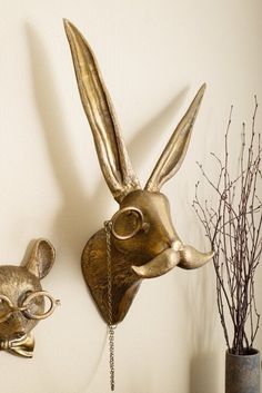 two metal rabbit head masks on a wall next to a vase with branches in it