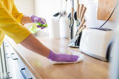 a person in yellow shirt and purple gloves cleaning counter