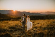 a bride and groom walk through the grass at sunset on their wedding day in the mountains