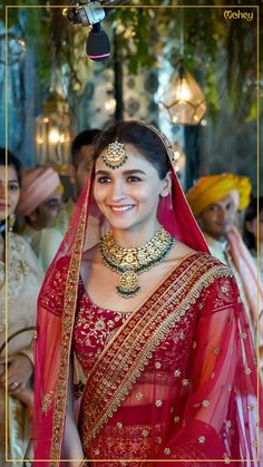 a woman in a red sari and gold jewelry smiles for the camera while others look on