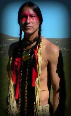 a native american man with red paint on his face and chest standing in the grass