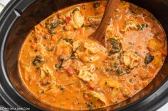 a crock pot filled with tortellini shells and spinach in tomato sauce