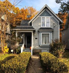 a gray house with white trim and two windows in the front yard surrounded by hedges