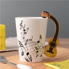 a coffee cup with music notes on it and a guitar in the mug next to it