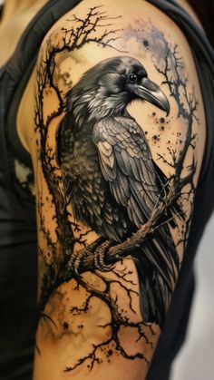 a woman with a black and grey tattoo on her arm is holding a crow perched on a tree branch