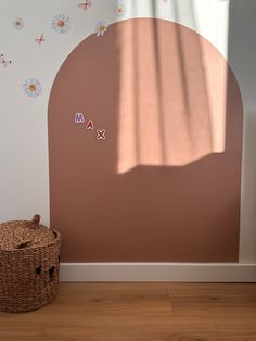 a brown basket sitting on top of a wooden floor next to a wall with flowers