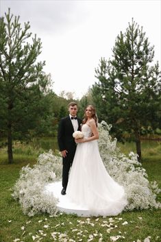 a bride and groom posing for a photo in front of white flowers on the grass