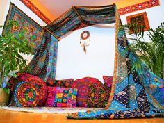 a bed covered in lots of different colored blankets and pillows next to a potted plant