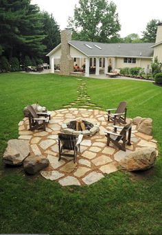 a stone fire pit in the middle of a yard with chairs and tables around it