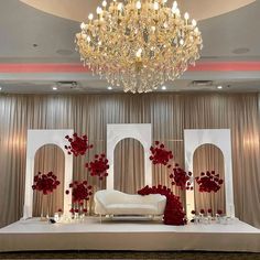 a white couch sitting under a chandelier in front of a stage with red flowers on it