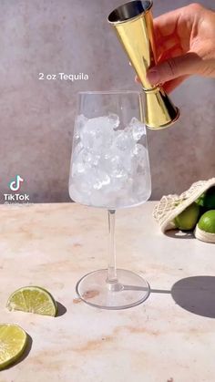 a person is pouring some ice into a glass with limes on the table next to it