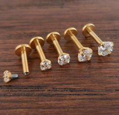 four gold screws and two diamond studs on a wooden surface