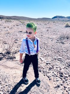 a young boy with green hair wearing suspenders and a white shirt in the desert