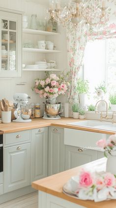 a kitchen with white cabinets and pink flowers on the window sill above the sink