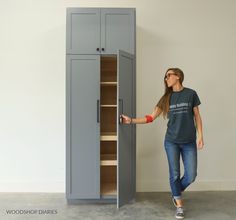 a woman standing next to a tall gray cabinet with doors open and she has her hand on the door