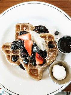 a waffle topped with berries, blueberries and whipped cream on a white plate