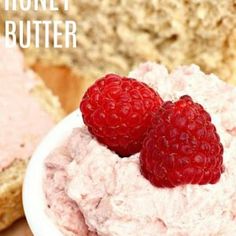 two raspberries sit on top of a bowl of cream cheese next to bread